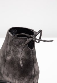 Černé semišové kotníkové boty s kulatou špičkou, zdobené mašlí a měkkou texturou. Boční otvor s podrobným prošíváním.