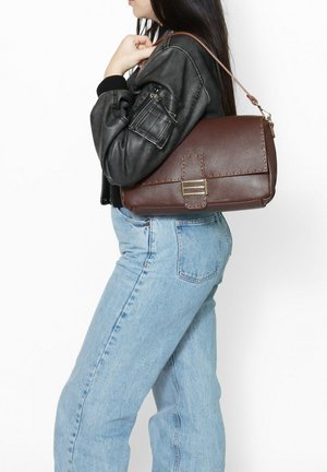 Borsa a spalla in pelle marrone con una finitura testurizzata, dotata di chiusura a pattina e hardware in metallo. Indossata in modo casual su una giacca di pelle nera.