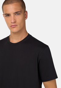 Juodas trumpomis rankovėmis marškinėliai su apvalia iškirpte, pagaminti iš lygaus medvilnės, su minimaliais siūlių detalėmis ir prigludusia forma.