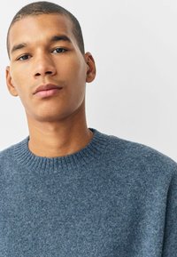 Blauwe gebreide trui met een ronde halslijn en geribde afwerking. De stof lijkt zacht met een getextureerde, pluizige afwerking.