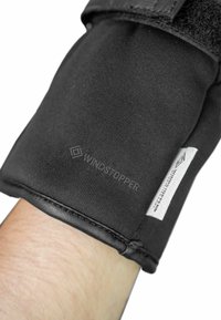Schwarzer Handschuh mit Windstopper-Branding, ausgestattet mit einem strukturierten Stoff und einem glatten Lederbund, der sicher mit einem Klettverschluss befestigt ist.