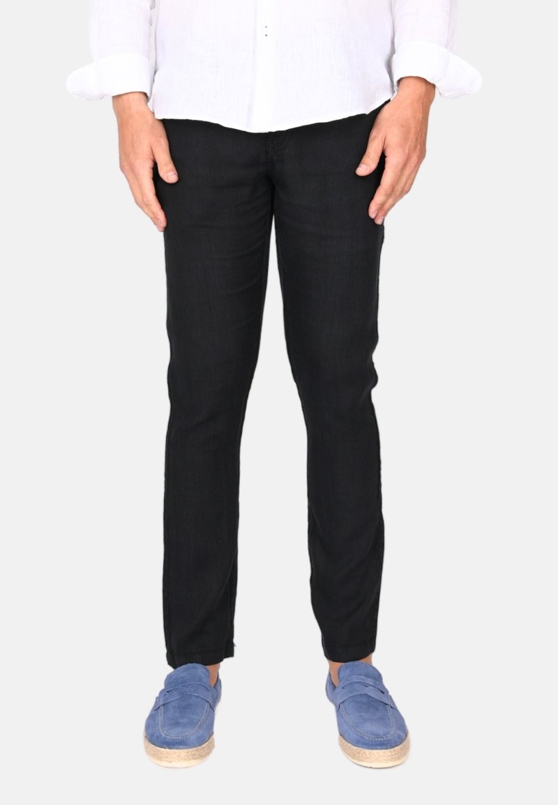 Schwarze, schmal geschnittene Jeanshose mit subtiler Textur. Kombiniert mit blauen Slippern mit Jutesohle.