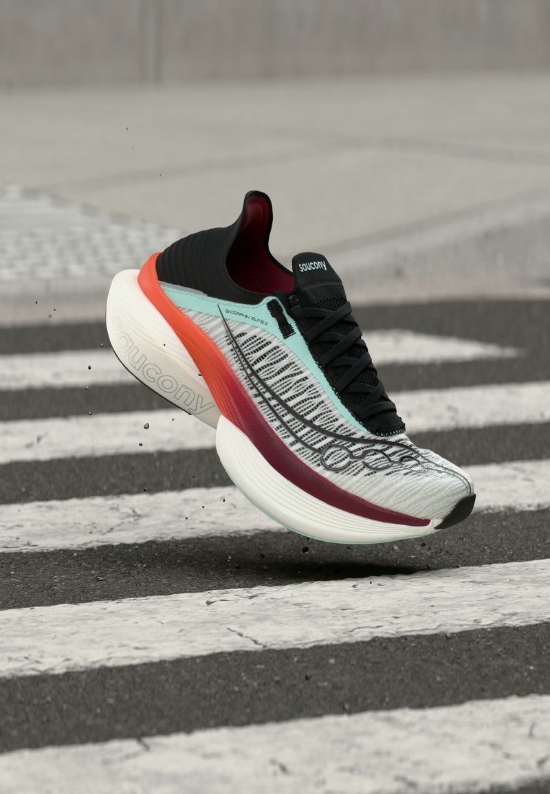 Baltas ir juodas Saucony bėgimo batelis su raudonomis ir turkio spalvos detalėmis pakeltas virš juodai baltos perėjos.