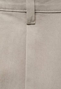 Tissu en coton beige avec une texture fine, comportant une couture verticale et une passante de ceinture. Design à coupe droite, adapté pour une tenue décontractée ou formelle.