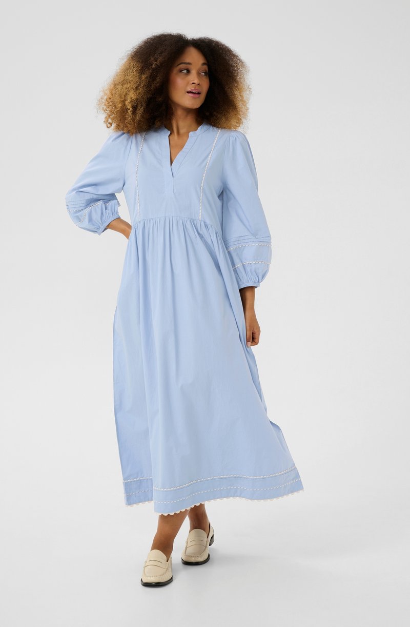 Light blue, long-sleeve dress with a v-neck, gathered waist, and scalloped hem. Features decorative stitching and loose, puffed sleeves.