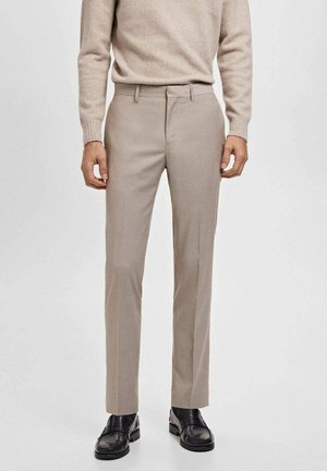 Beige op maat gemaakte broek met een slim fit, vlakke voorkant en subtiele textuur. Gegdraag in combinatie met een lichte trui en zwarte schoenen.