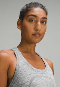 Gray athletic tank top with a scoop neckline, soft texture, and wide straps. Detail of logo visible on fabric.