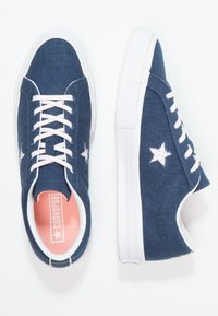 Námořnické plátěné tenisky s bílou gumovou podrážkou a růžovými akcenty. Mezi vlastnostmi jsou hvězdicové vzory na bocích a světle růžové tkaničky.