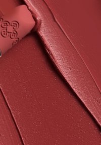 Matt läppstift i en djup röd nyans, krämig konsistens och slät finish, tillsammans med en delvis synlig applicator i en elegant design.