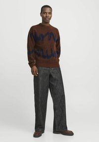 Brauner Strickpullover mit blauem wellenförmigen Muster. Kombiniert mit lockeren, dunklen Jeans und braunen flachen Schuhen. Einfacher runder Ausschnitt und gerippte Bündchen.