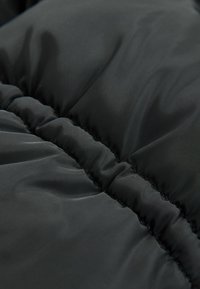 Giubbotto imbottito nero, caratterizzato da una texture trapuntata con cuciture visibili e cuciture arricciate, che mette in mostra una finitura morbida e opaca.