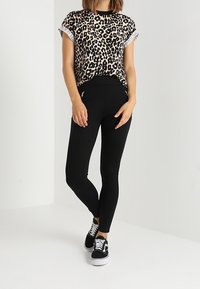 Musta legginsit yhdistettyinä löysään leopardikuvioiseen puseroon, jossa on pussitaskut. Asusteena mustat lenkkarit.