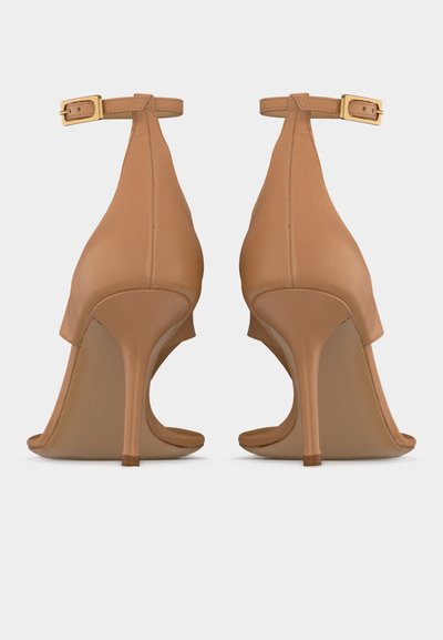 Ζευγάρι ταμπά ψηλοτάκουνα σανδάλια με λουριά στον αστράγαλο και χρυσή αγκράφα, εμφανιζόμενα από πίσω σε λευκό φόντο.