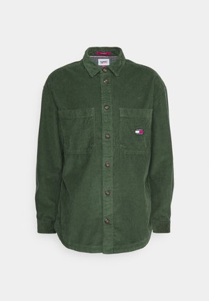 Zielona koszula sztruksowa na guziki z kołnierzykiem, dwoma kieszeniami na piersi oraz małą naszywką z logo Tommy Jeans na prawej kieszeni.