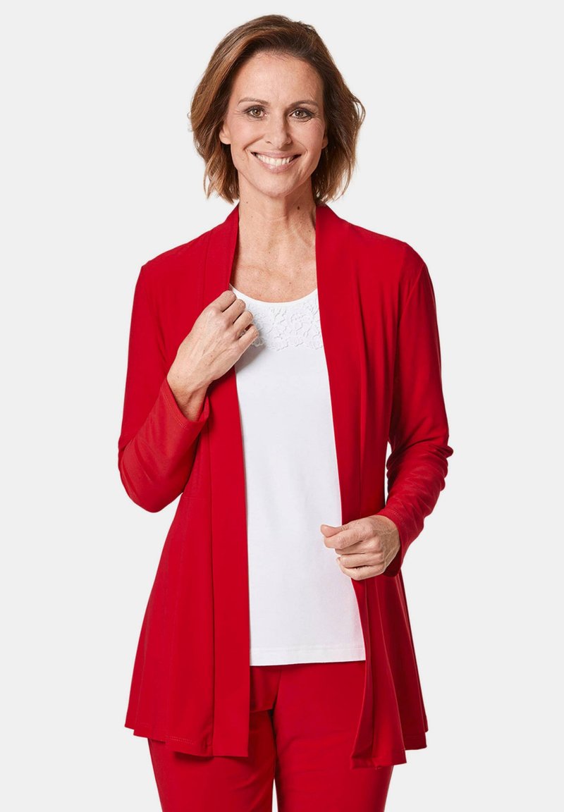 Rode lichte cardigan met lange mouwen, gedrapeerd ontwerp aan de voorkant, gedragen over een wit shirt. Gladde textuur, geen zichtbare patronen of accenten.