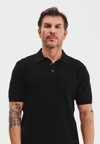 Czarny krótki rękaw koszulka polo z teksturowanym wzorem, z listwą z dwoma guzikami i kontrastowym czarnym kołnierzykiem. Minimalistyczny design.