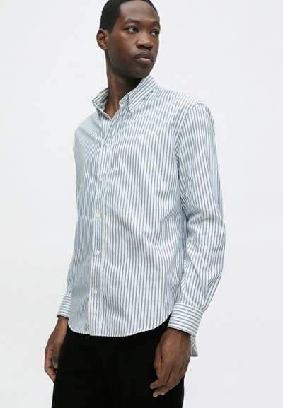Cămașă cu dungi, albă și albastră deschisă, cu guler clasic, mâneci lungi și tiv curbat. Dispune de nasturi vizibili și logo-ul brandului.