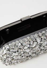 Clutch rigido nero con chiusura metallica. La parte anteriore è decorata con strass argentati e accenti di perle su una superficie texturizzata.
