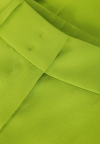 Neon zelená tkanina s texturovanou vazbou, obsahující překrývající se části a rovné švy. Materiál vypadá lehce a odolně.