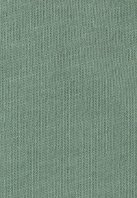 Piparmētru zaļa adīta auduma ar teksturētu virsmu, kas izceļas ar vienmērīgu ribu rakstu un smalkām diegām, rādīdama nelielas krāsas variācijas.