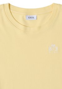 T-shirt jaune clair à col rond avec étiquette "CECIL" au col et petit texte blanc "BE KIND" avec broderie de palmier sur la poitrine.