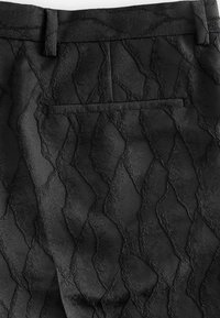 Black textured pants featuring a wave-like pattern and a single back pocket, made from a soft, fabric material with a subtle sheen.