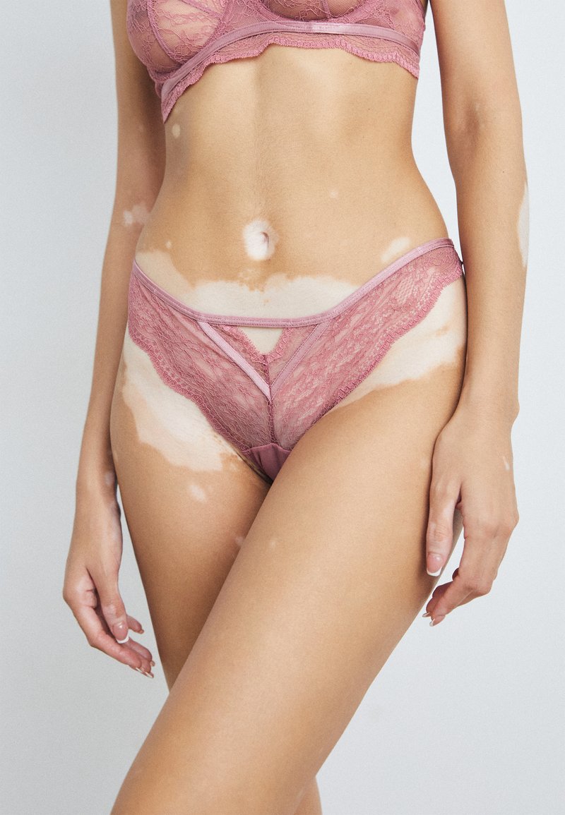 Lichtroze kant bralette en bijpassende string, met ingewikkelde bloemmotieven en zachte elastische afwerking, die een delicate, getextureerde uitstraling benadrukt.