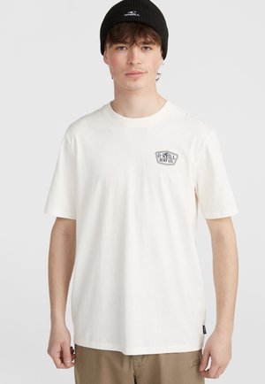 Valge puuvillane T-särk lühikeste varrukatega, millel on rindkere kohal väike must logo. Kandmine khaki põllukatega ja musta beanie'ga.