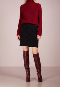 Burgundský žebrovaný rolák kombinovaný s černou sukní ke kolenům a lesklými, burgundskými koženými vysokými botami. Hladká textura, přiléhavý design.