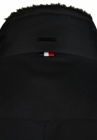 Col de veste noir texturé avec une bordure en fausse fourrure et une petite étiquette en tissu rouge, blanc et bleu sous le nom de la marque embossé "HECHTER".