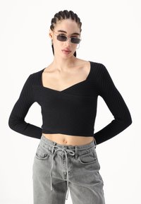 Top corto negro de canalé con escote en V y mangas largas, combinado con pantalones gris claro con cordón. Diseño sencillo, tejido texturizado.