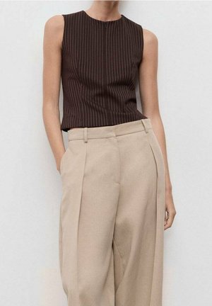 Haut sans manches marron foncé à fines rayures, associé à un pantalon beige taille haute large, les mains reposant dans les poches.
