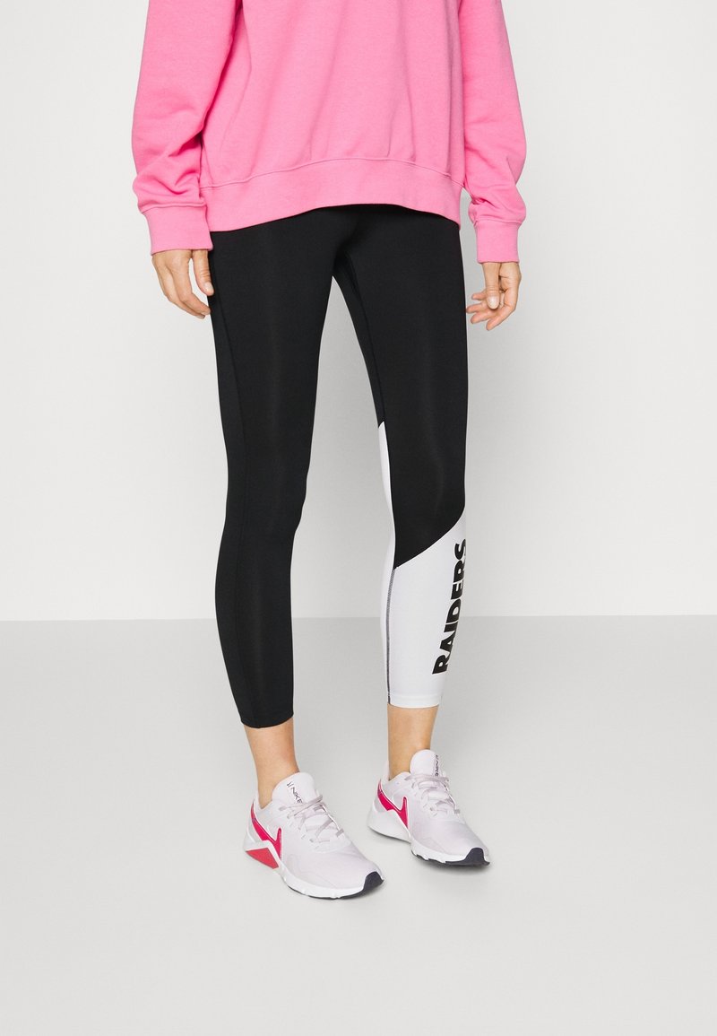 Personne portant un legging noir et blanc avec le texte "RAIDERS" sur le mollet, un sweat-shirt rose et des baskets blanches avec des accents roses.