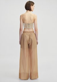 Dwuczęściowy zestaw składający się z przezroczystych, beżowych spodni w szerokie nogawki oraz dopasowanego topu na cienkich ramiączkach z fakturowanym, prążkowanym wzorem.