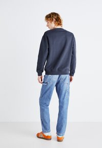 Navy sweatshirt with ribbed cuffs and hem, paired with light blue distressed jeans featuring multiple pockets. Bright orange sneakers.