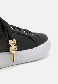 Black synthetic sneaker with a smooth finish, gold eyelets, black laces, and a heart-shaped charm displaying "LOVE MOSCHINO." White rubber sole.