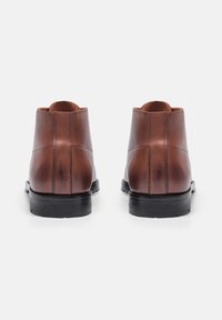 Bottines en cuir marron avec une texture lisse, à bouts ronds et une semelle en caoutchouc noir. Les détails de couture sur le côté ajoutent un intérêt visuel.