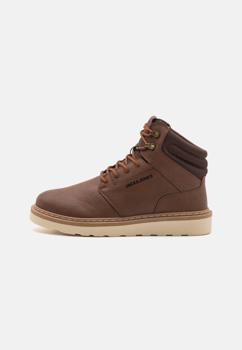 Bruine leren enkelbo boots met een gewatteerde kraag, voorzien van bruine veters, messing oogjes en een lichte rubberen zool. Logo zichtbaar op de zijkant.