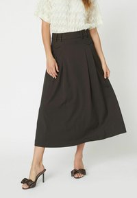 Schwarzer, plissierter Midirock mit hoher Taille, seitlichen Taschen und einer glatten Textur. Kombiniert mit offenen Schuhen mit Absatz, die eine Schleifenakzent haben.