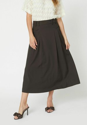 Black pleated midi skirt with a high waist, side pockets, and a smooth texture. Worn with open-toed heels featuring a bow accent.