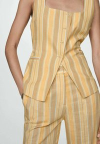 Linen two-piece set featuring a sleeveless, square-neck top with buttons and striped design in yellow, beige, and light blue. Pants have back pockets.