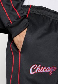 Jambiere atletice negre cu dungi accent roșii. Include un buzunar lateral și cuvântul "Chicago" brodat în albastru. Material moale și design cu picior tapered.