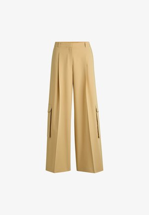 Beige kengät leveät housut, valmistettu sileästä kankaasta, jotka sisältävät etu taitokset ja kaksi sivupussit, joissa on läpät. Mukautettu vyötärö sopivuutta varten.