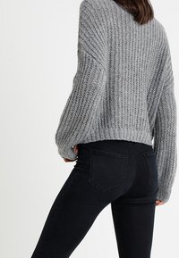 Grey knitted sweater with a loose fit and ribbed texture, paired with high-waisted black jeans featuring back pockets.