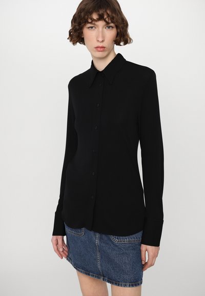 Svart langermet skjorte med knapper og spiss krage, kombinert med et blått denimskjørt med frontlommer og lett falm.