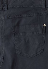 Pantalons en denim de coton bleu marine foncé avec une poche arrière présentant des coutures visibles et un accent de bouton métallique. Texture lisse.