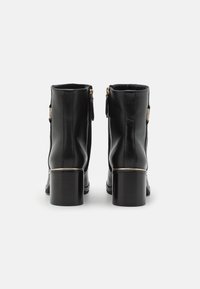 Botas de cuero negro hasta el tobillo con punta redonda, cremalleras laterales y un tacón grueso que presenta un acento dorado en la base.