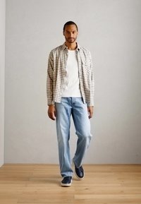 Uformell antrekk med en rutete skjorte i lysegrå og brun, hvit T-skjorte, lyseblå jeans og marineblå sneakers, på tregulv.