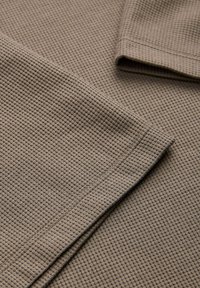 Υφασμάτινο ύφασμα μπεζ με υφή βάφλας και ορατές ραφές, διπλωμένο για να δείξει υφή και λεπτομέρειες ρεβέρ περιοχής μανικιού ρούχου.