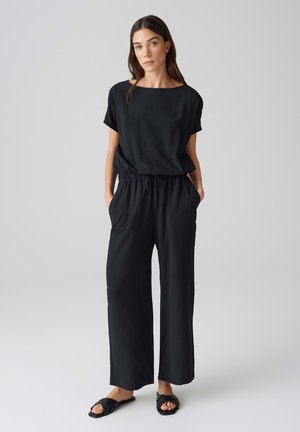 Completo due pezzi nero composto da una maglietta ampia a maniche corte con scollatura rotonda e pantaloni larghi a vita elastica con tasche laterali.